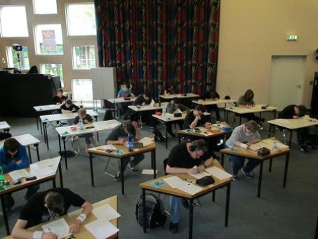 12 Schüler sitzen an Einzeltischen in der Aula und arbeiten ihre Prüfungen durch